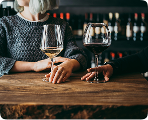 Two wine glasses, one filled with white wine and the other with red wine, on a wooden table, with blurred wine bottles in the background, symbolizing wine appreciation and storage solutions for wine cellars.