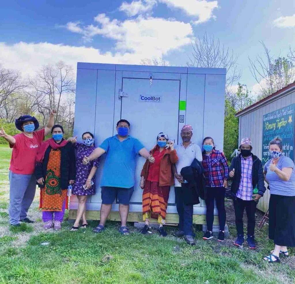 Group of farmers, including refugees from Burma and Bhutan, celebrating beside a CoolBot cold storage unit, promoting fresh produce access and community food security in Nashville.