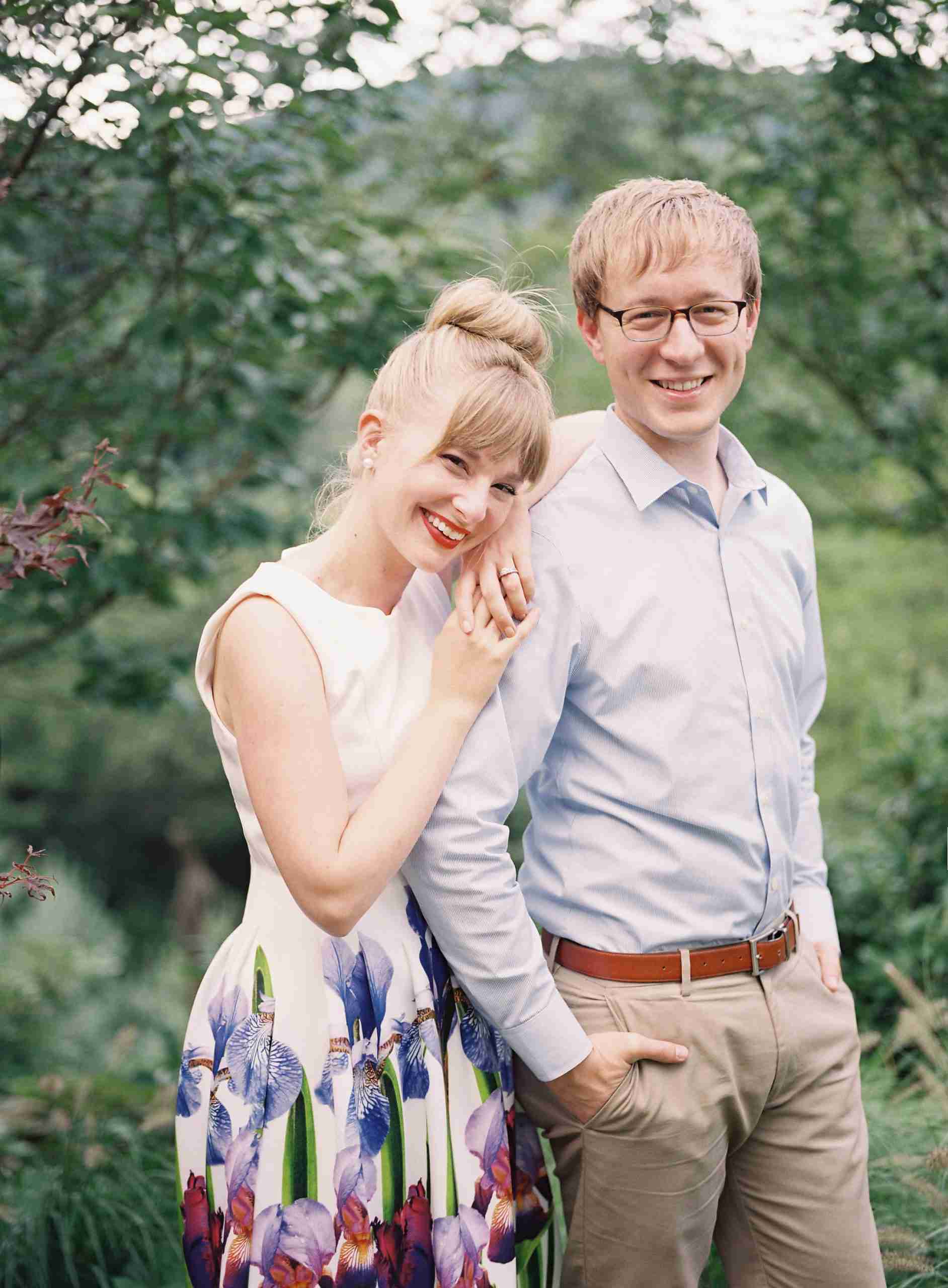 Couple posing outdoors, smiling, with the woman in a floral dress and the man in a light blue shirt, representing Team Flower's community and support in the floral industry.